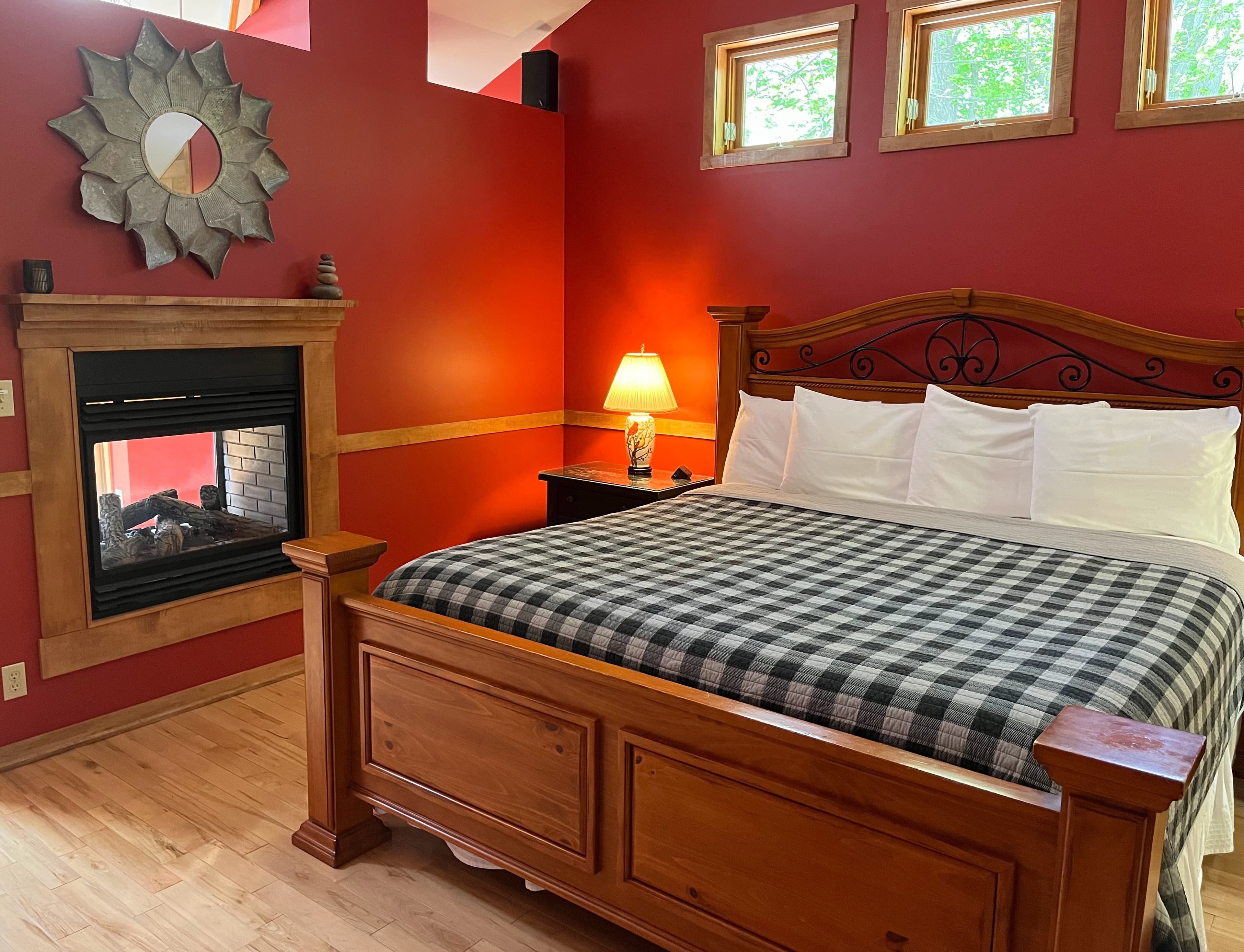 View of King Size bed against a red wall under three square windows looking into the tree tops