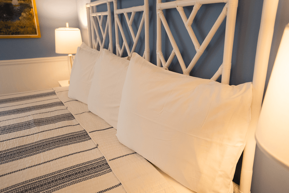 A neatly made bed with white pillows and a patterned blanket, set against a blue wall.